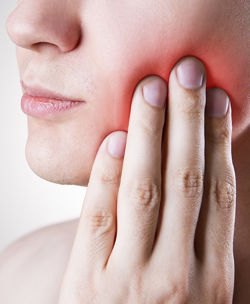 Patient in need of wisdom tooth extractions holding cheek in pain