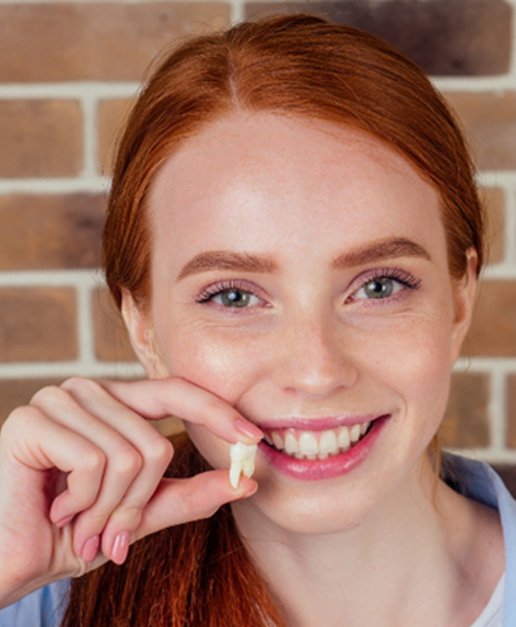 A smiling woman holding an extracted tooth between her fingers