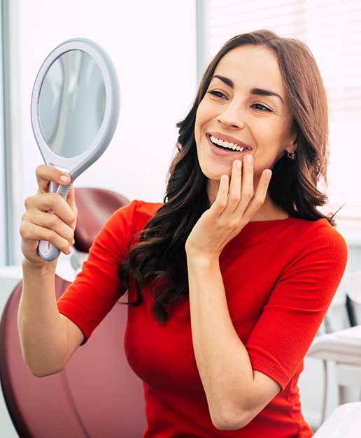 Woman looking at her new porcelain veneers during cosmetic dentistry visit