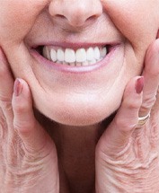 a woman holding her cheek and smiling with dentures