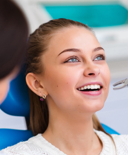 Woman in dental chair looking up as dentist approaches with forceps to extract tooth