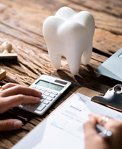 Hands on calculator and invoice on wooden desk with large model tooth, stamp, and laptop