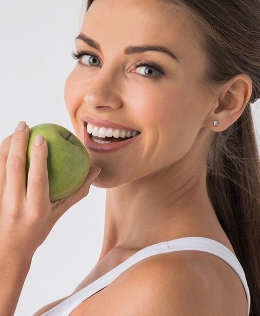 Woman eating an apple after dental implant supported tooth replacement