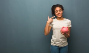 woman with dental insurance holding a piggy bank and pointing to her smile 