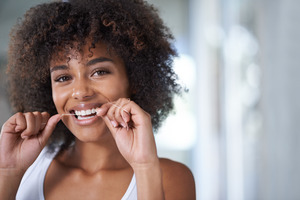 Woman in white shirt flossing her teeth