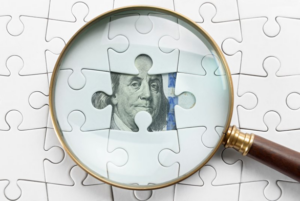 Magnifying glass hovering over money that’s hidden behind puzzle pieces